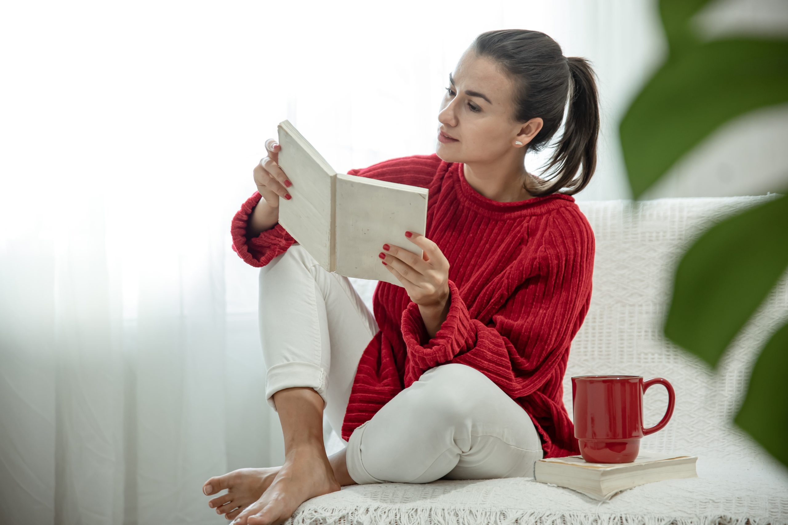 A young woman in a red sweater with a book in her hands is sitting on the couch. A young woman in a red sweater with a book in her hands is sitting on the couch.